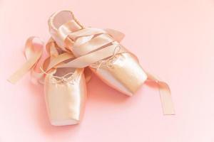 New pastel beige ballet shoes with satin ribbon isolated on pink background. Ballerina classical pointe shoes for dance training. Ballet school concept. Top view flat lay, copy space photo