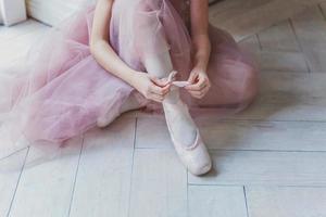 Ballerina hands puts pointe shoes on leg in dance class photo