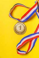 Simply flat lay design winner or champion gold trophy medal isolated on yellow colorful background. Victory first place of competition. Winning or success concept. Top view. photo