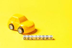 Simply design yellow toy car and inscription DELIVERY word isolated on yellow colorful background. Internet shopping online purchase e-commerce packages delivery service concept Copy space photo
