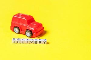 Simply design red toy car and inscription DELIVERY word isolated on yellow colorful background. Internet shopping online purchase e-commerce packages delivery service concept Copy space photo