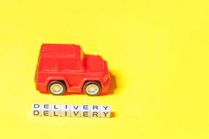 Simply design red toy car and inscription DELIVERY word isolated on yellow colorful background. Internet shopping online purchase e-commerce packages delivery service concept Copy space photo