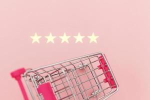 Small supermarket grocery push cart for shopping toy with wheels and 5 stars rating isolated on pastel pink background. Retail consumer buying online assessment and review concept. photo