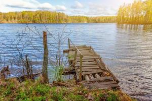 Forest lake or river on summer day and old rustic wooden dock or pier photo