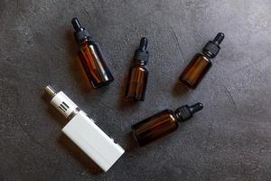 Vaping device e-cigarette electronic cigarette and liquid bottles on dark black stone shale background. Vape device for alternative smoking. Vaping shop concept. Gadget for vaper. Vaping accessories. photo
