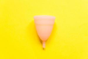 Simply minimal design pink menstrual cup Isolated on yellow background. Woman modern alternative eco gynecological hygiene in menstruation period. Container for blood. Flat lay top view, copy space photo