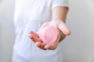 Woman hand holding pink menstrual cup isolated on white background. Woman modern alternative eco gynecological hygiene in menstruation period. Container for blood in girl hand. photo