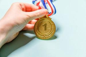 Simply flat lay design hand holding winner or champion gold trophy medal isolated on blue colorful background. Victory first place of competition. Winning or success concept. Top view copy space. photo