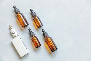 Vaping device e-cigarette electronic cigarette and liquid bottles on concrete stone grey background. Vape device for alternative smoking. Vaping shop concept. Gadget for vaper. Vaping accessories. photo