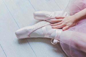 Ballerina hands puts pointe shoes on leg in dance class photo