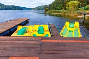 Pedal boats or paddle boats catamarans station. Yellow water bicycles locked at lake marina dock pier on sunny summer day. Summer leisure activity outdoors. photo