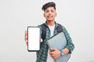 Young indian student holding file and showing smartphone screen on white background. photo