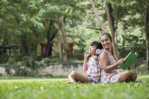 Mother and daughter reading a fairytale to her daughter listen sound with headphone in the park photo