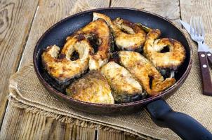 Old frying pan with fried fish on wooden table. photo