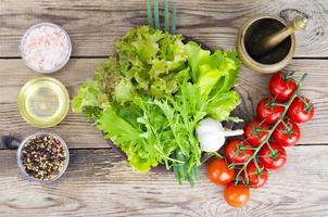 Green salad ingredients organic lettuce, cherry tomatoes, spices and olive oil on wooden background. photo