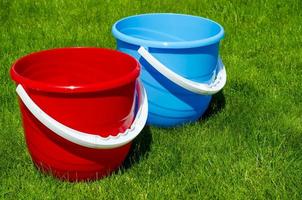 Colored plastic garden buckets on background of green grass photo