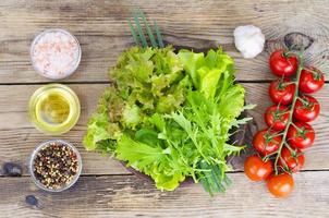 Green salad ingredients organic lettuce, cherry tomatoes, spices and olive oil on wooden background. photo