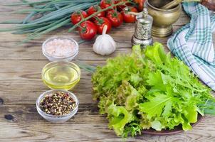 Green salad ingredients organic lettuce, cherry tomatoes, spices and olive oil on wooden background. photo