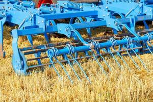 una grada de metal cilíndrica de varias filas en azul contra un campo amarillo cosechado a la luz del sol. de cerca. foto