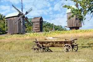An old wooden cart with hay on the background of a summer landscape with old wooden mills. photo