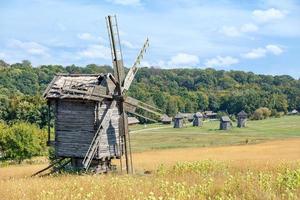Antique wooden windmill against the backdrop of a rural antique summer landscape with blue sky and dense forest. photo
