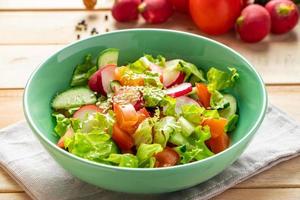 Recipe for vegetable salad with tomatoes, cucumbers and radishes. Seasonal dish on wooden background. photo