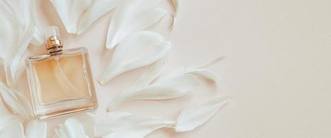 Perfume bottle and flower petals on pastel beige background. Natural cosmetics with aromatic oil. photo