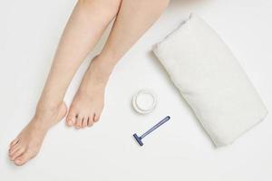 Woman leg, towel, razor and cosmetic cream on white background