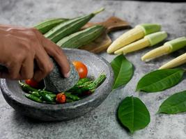 las manos están moliendo chiles y tomates con un mortero para hacer salsa de chile. concepto de preparación de comida vegetariana foto