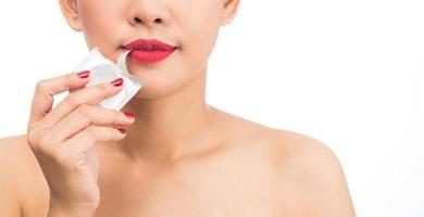mujer joven chica asiática boca desgarrada sobre condón sobre fondo blanco foto