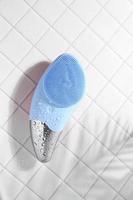 Blue sonic facial brush on white tile with water drops photo