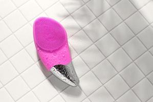 Pink facial sonic brush for massage on white tile with water drops photo