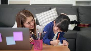 mãe e filha felizes asiáticas estão usando laptop para estudar online via internet em casa. conceito de e-learning durante o tempo de quarentena. video