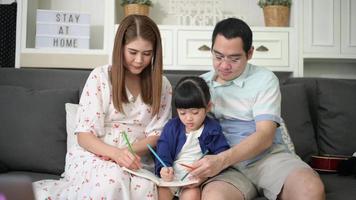 feliz pai asiático ensinando filhinha fofa a fazer lição de casa e desenhar juntos em casa.