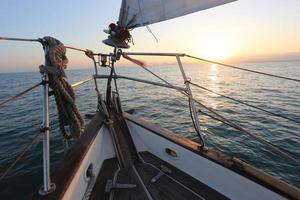 puesta de sol sobre la proa con un velero en marcha foto