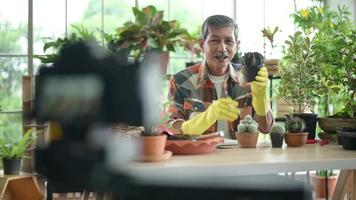 un entrepreneur senior travaillant avec une caméra présente des plantes d'intérieur lors d'une diffusion en direct en ligne à la maison, vendant un concept en ligne