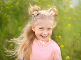 Cute little smiling blonde girl with chamomile in her hairdress and in her teeth photo