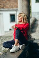 mujer joven feliz sentada en el fondo urbano tomando el sol en otoño foto