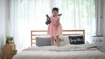 feliz linda garota se divertindo pula e brinca na cama branca no quarto video