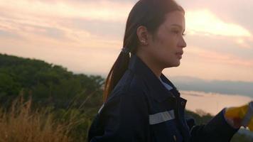 a woman engineer is putting a protective helmet on her head at sunset. video