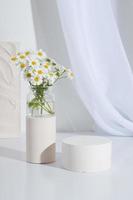 zócalo cor cilíndrico vacío con flores de manzanilla sobre un fondo blanco. fondo de pie de producto de estante en blanco foto