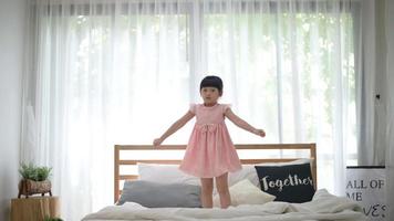 happy cute girl having fun jumps and plays on white bed in bedroom video