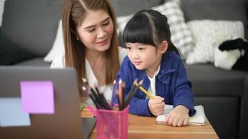 madre e hija felices asiáticas están usando una computadora portátil para estudiar en línea a través de Internet en casa. concepto de aprendizaje electrónico durante el tiempo de cuarentena. video