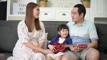 little girl singing and playing guitar with her family while sitting on sofa at home