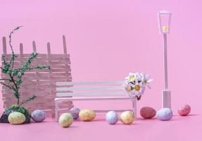 Concept for Easter card, banner or invitation. On a pink background, a white bench with eggs and decorations closeup with copy space. photo