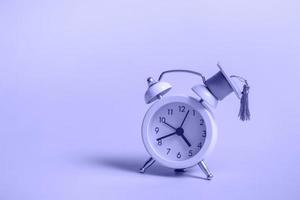 Yellow alarm clock with graduation cap on very peri background closeup with copy space photo