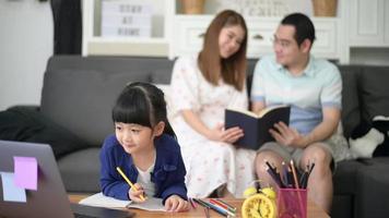 la figlia asiatica felice sta usando il laptop per studiare online via Internet mentre il genitore è seduto sul divano a casa. concetto di e-learning video