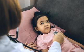 niña asiática una mujer dormía en una almohada en el sofá para una doctora usando estetoscopio en un latido del corazón en casa. foto
