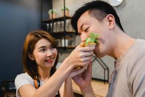 Beautiful happy asian couple are feeding each other in the kitchen. Young asian man and woman have romantic time while staying at home. Couple lifestyle at home concept. photo