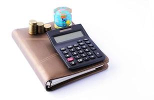 concepto de negocio con calculadora y pila de monedas de dinero en el libro de notas de negocios sobre fondo blanco